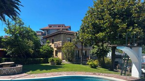 Ein Schwimmbecken mit Steinbord, einer gepflegten Rasenfläche und ein zweistöckiges Gebäude mit Balkon im Hintergrund.