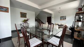 Amplia sala de estar con una mesa de comedor de vidrio rodeada de sillas, una escalera que lleva a otro nivel y una zona de estar acogedora con un sofá y sillones.