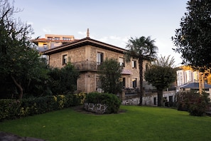 Un edificio a due piani con facciata in pietra, un balcone e un giardino curato.