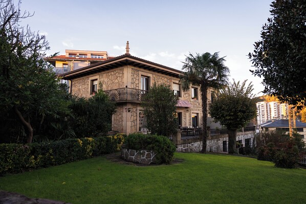 Un edificio de dos pisos con fachada de piedra, un balcón y un jardín bien cuidado.