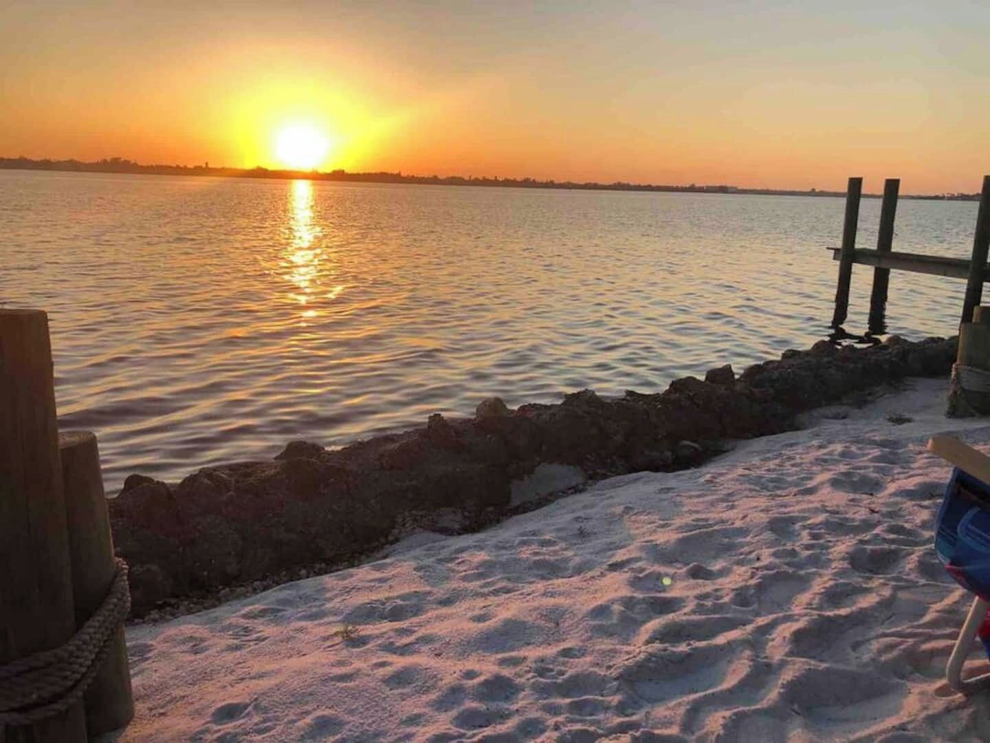 A sunset over a calm body of water with a wooden pier and a sandy beach.