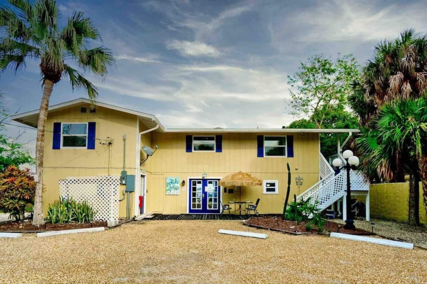 A two-story building with a front patio, a blue door, and a staircase leading to the upper level.