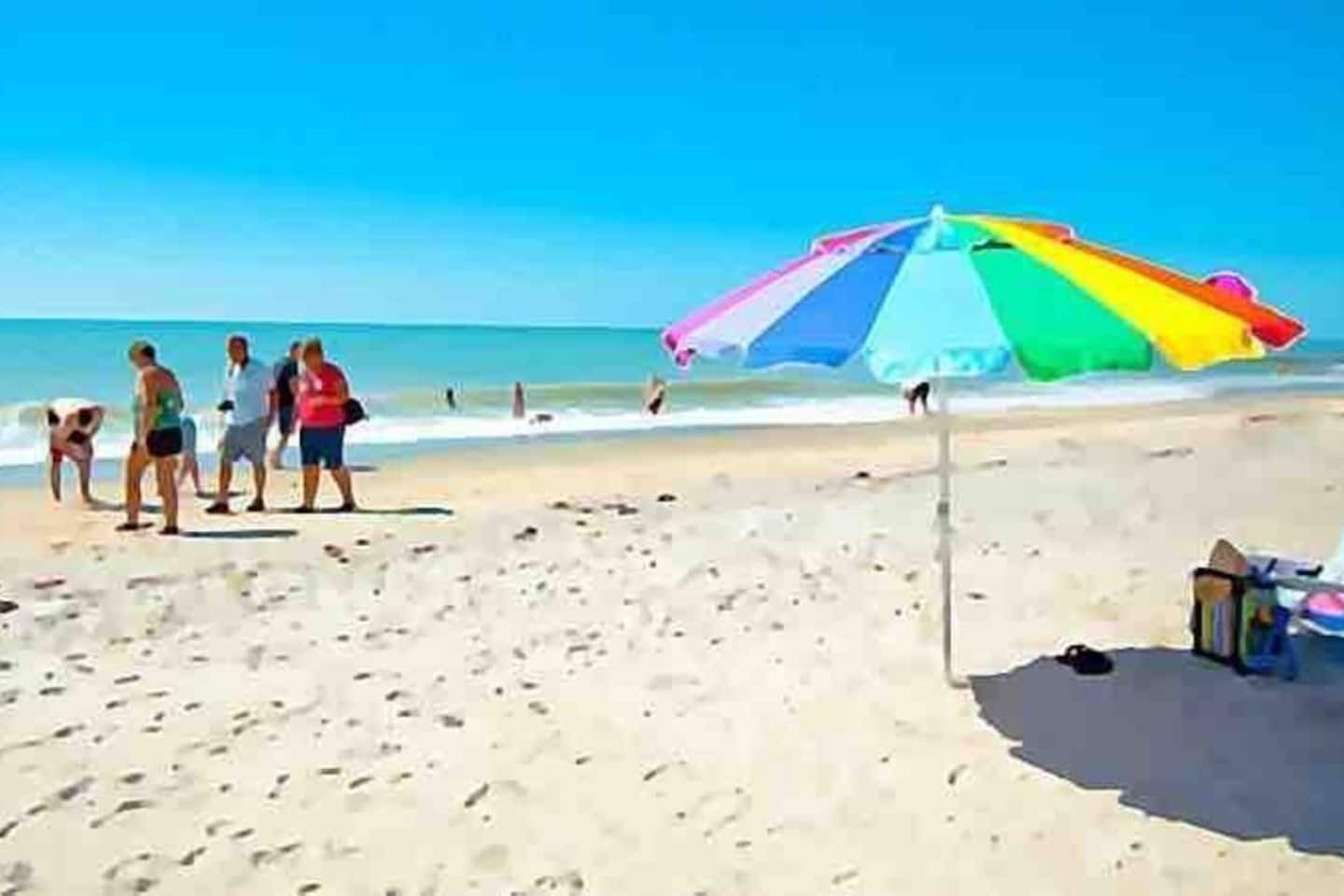 Escena de platja amb un parasol colorit i empremtes a la sorra.