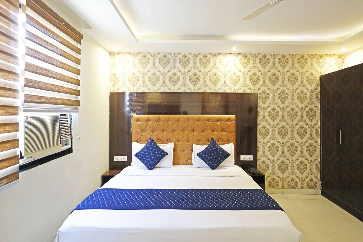 A hotel room with a large bed, a wooden headboard, patterned wallpaper, and a wardrobe.