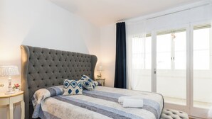 A bedroom with a tufted headboard, a striped bedspread, and a view of the outside through a glass door.