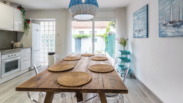 A modern kitchen with a wooden table, hanging blue light fixture, and nautical paintings.