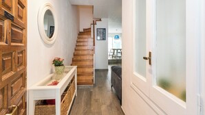 A hallway with a wooden staircase, a white console table with a vase, and a door with frosted glass.