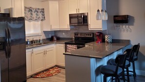 A modern kitchen with white cabinets, stainless steel appliances, a central island with bar stools, and a ceiling light fixture. - LAKEFRONT End Unit Condo at 3 Seasons @ 21MM  (Osage Beach)
