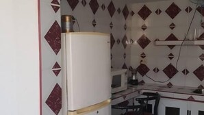 Een compacte keuken met een koelkast, magnetron en een klein eethoekje met krukken.