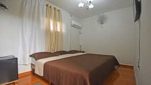 Een slaapkamer met een bed, een bureau, een stoel, een airconditioner, een ventilator en een vloerkleed.