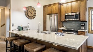 A kitchen with wooden cabinets, a stainless steel refrigerator, a microwave, and a large clock on the wall. - Phoenix 108 4 Bedroom Townhouse by RedAwning (Steamboat Springs)