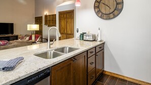 A kitchen with a granite countertop, stainless steel sink, wooden cabinets, a clock, and a dining area with a table and chairs. - Phoenix 108 4 Bedroom Townhouse by RedAwning (Steamboat Springs)