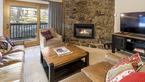 A cozy living room with a stone fireplace, leather sofas, a wooden coffee table, and a TV on a wooden stand. - Phoenix 108 4 Bedroom Townhouse by RedAwning (Steamboat Springs)