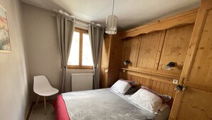 A bedroom with a bed, a chair, wooden paneling, a radiator, and a window with curtains. - Apartment for 4 people on the slopes (Lanslevillard)