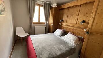 Een slaapkamer met een bed, een stoel, houten lambrisering, een radiator en een raam met gordijnen.