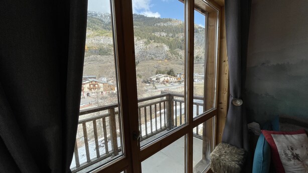 A room with large windows offering a view of a mountainous landscape and a small building. - Apartment for 4 people on the slopes (Lanslevillard)