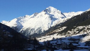 A snow-covered mountain with a clear sky. There are buildings in the foreground with snow on their roofs. - Apartment for 4 people on the slopes (Lanslevillard)
