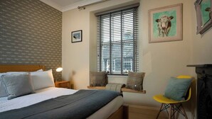 A bedroom with a bed, bedside tables, a window with blinds, a chair, and a fireplace. - Central Home with Parking & Sky TV by LetMeStay (Cumbria)