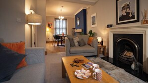A living room with a sofa, a coffee table with books and a plate of pastries, a fireplace, and a dining area in the background. - Central Home with Parking & Sky TV by LetMeStay (Cumbria)