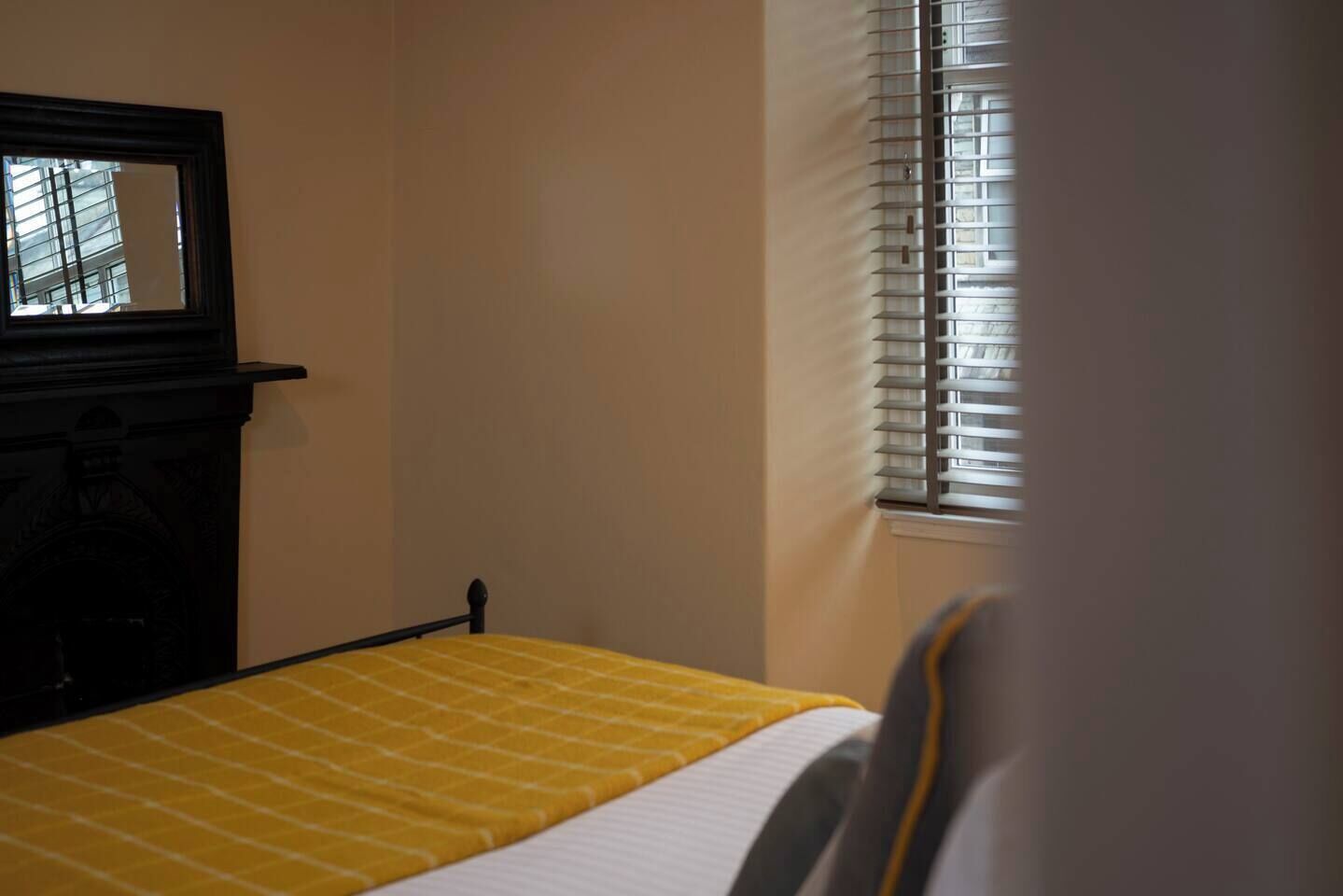 A room with a bed, a window with blinds, and a mirror on the wall.