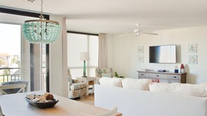 Una sala de estar moderna con un sofá blanco, una mesa de comedor con un bol de aperitivos, una araña y un televisor en la pared.