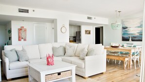 Una sala de estar amplia con un sofá blanco, una mesa de centro y un comedor con mesa y sillas de madera.