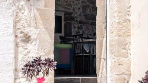 Un edificio de piedra con fachada rústica, una maceta con flores rosas y una vista parcial de un comedor en el interior.