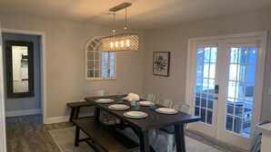 Une salle à manger avec une table en bois foncé dressée pour six personnes, un lustre et un grand miroir au mur.