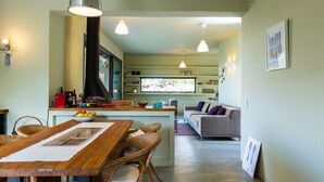 A modern kitchen with a central island, dining area with wicker chairs, and a living room with a sofa and a TV. - Tessera Villa, a Serene Escape in Nature with Pool (Spili, Rethymno)