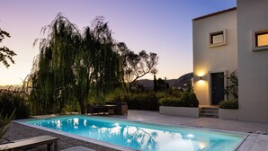 A swimming pool with lounge chairs and a modern building with steps leading to a door. - Tessera Villa, a Serene Escape in Nature with Pool (Spili, Rethymno)