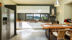 A modern kitchen with a large window, stainless steel appliances, and a dining area with wicker chairs. - Tessera Villa, a Serene Escape in Nature with Pool (Spili, Rethymno)