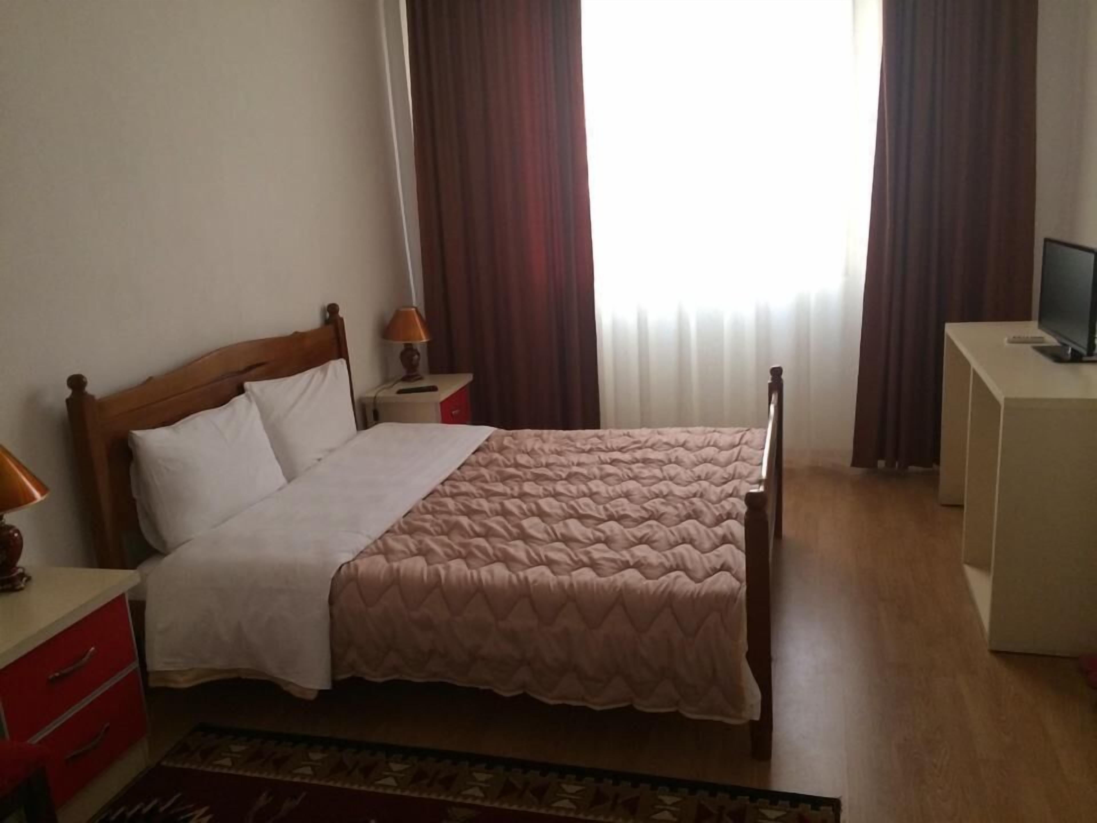 Een net opgemaakt bed met een houten hoofdbord, een nachtkastje met een lamp en een televisie op een standaard.
