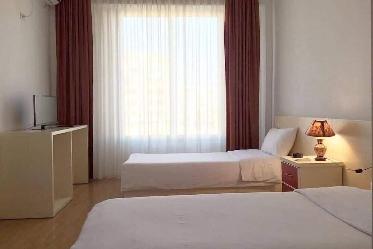 Ett hotellrum med två sängar, ett skrivbord, en lampa och en luftkonditioneringsanläggning.