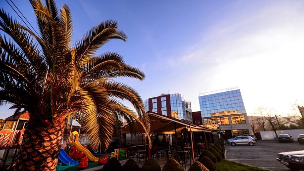 A commercial area with a palm tree, a playground, and a building with a glass facade.