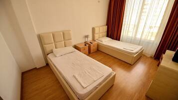 A hotel room with two beds, a nightstand, and a window with curtains.