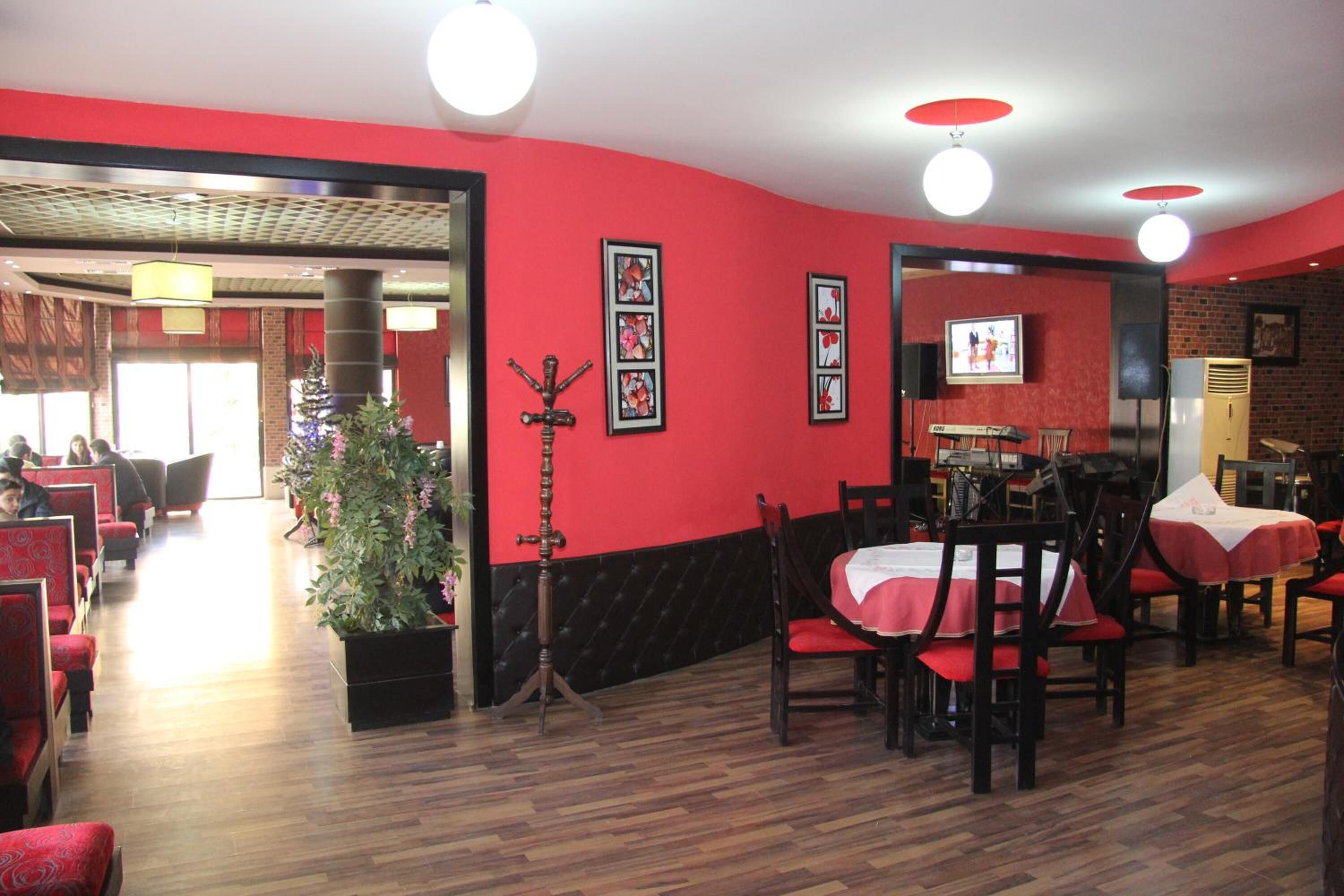 Ein Restaurant mit roten Wänden, Holzboden und rot-weißen Tischdecken. An den Wänden hängen gerahmte Bilder und in der Mitte steht ein Blumentopf.