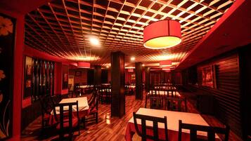 Un restaurante con suelo de madera, paredes rojas y techo con diseño de cuadrícula. Las mesas y sillas están dispuestas para comer.