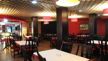 Interior de restaurante con mesas y sillas, paredes rojas y un techo con diseño.