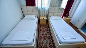 Habitación doble con dos camas individuales, una mesita de noche con lámpara, una mesita auxiliar y una alfombra decorativa.