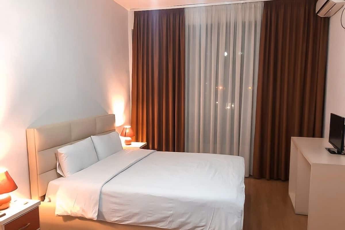 Ett hotellrum med en säng, sängbord, ett skrivbord och en tv.