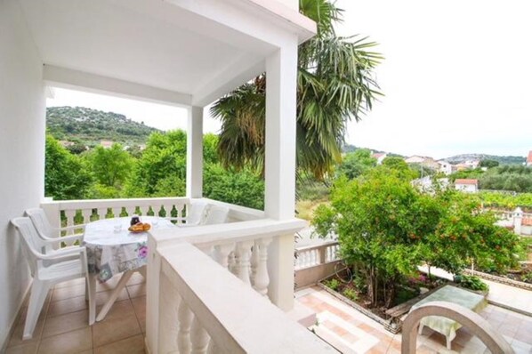 Un balcon avec une table et des chaises, donnant sur un paysage verdoyant et luxuriant ainsi que sur des maisons.