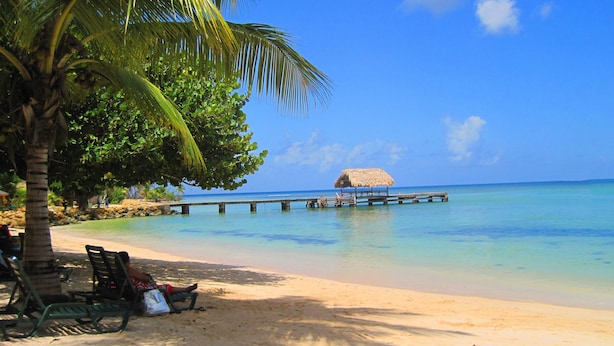 A beach with a wooden pier extending into calm waters, a thatched-roof hut, and a bench with a bag on it. - Private villa apartment with pool and within 15 minute walk to 3 beaches. (Bon Accord)