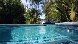 A clear swimming pool with blue patterned tiles, surrounded by lush greenery and a parked car. - Private villa apartment with pool and within 15 minute walk to 3 beaches. (Bon Accord)