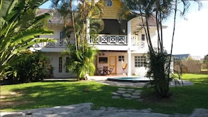 A two-story house with a balcony, surrounded by a well-maintained lawn and palm trees. - Private villa apartment with pool and within 15 minute walk to 3 beaches. (Bon Accord)