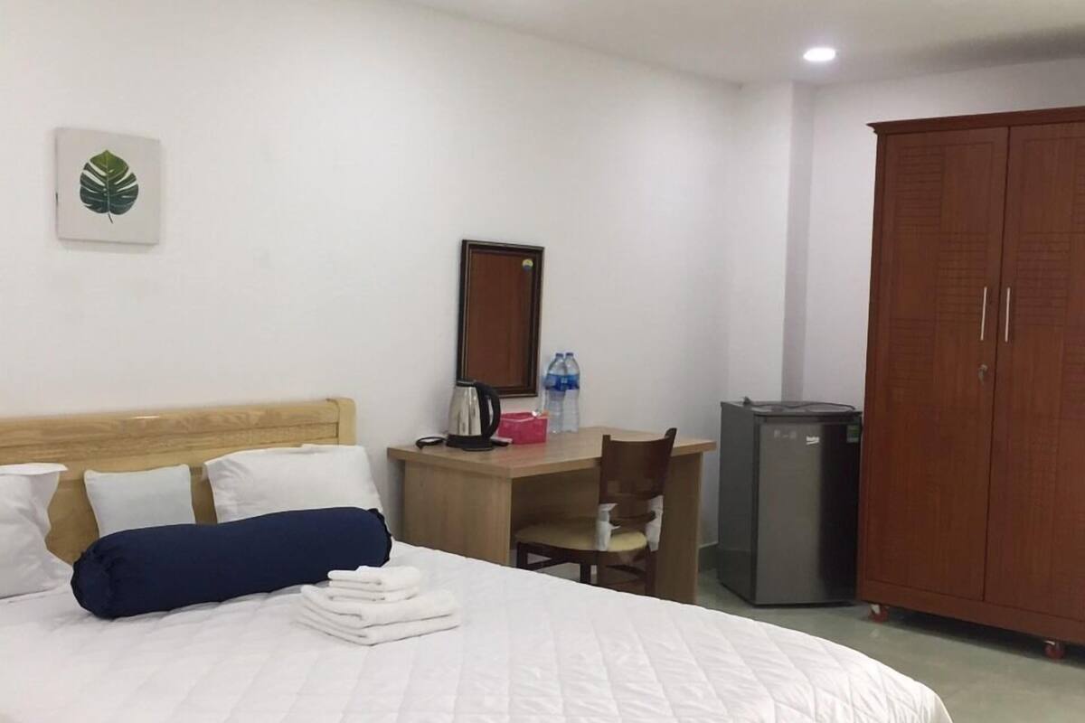 Une chambre d’hôtel équipée d’un lit, d’un bureau, d’une chaise, d’une armoire et d’un petit réfrigérateur.