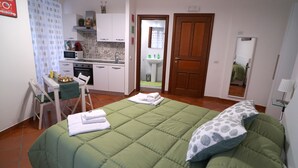 A compact room with a bed, a small kitchenette, a chair, and a door leading to a bathroom. - Naporà (Naples)