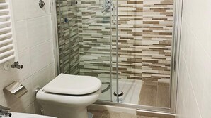 A modern bathroom with a glass-enclosed shower, two toilets, and a bidet. - Naporà (Naples)