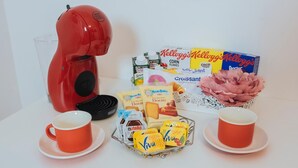A breakfast setup with a red coffee maker, two cups of coffee, a basket of pastries, and various breakfast items. - Naporà (Naples)