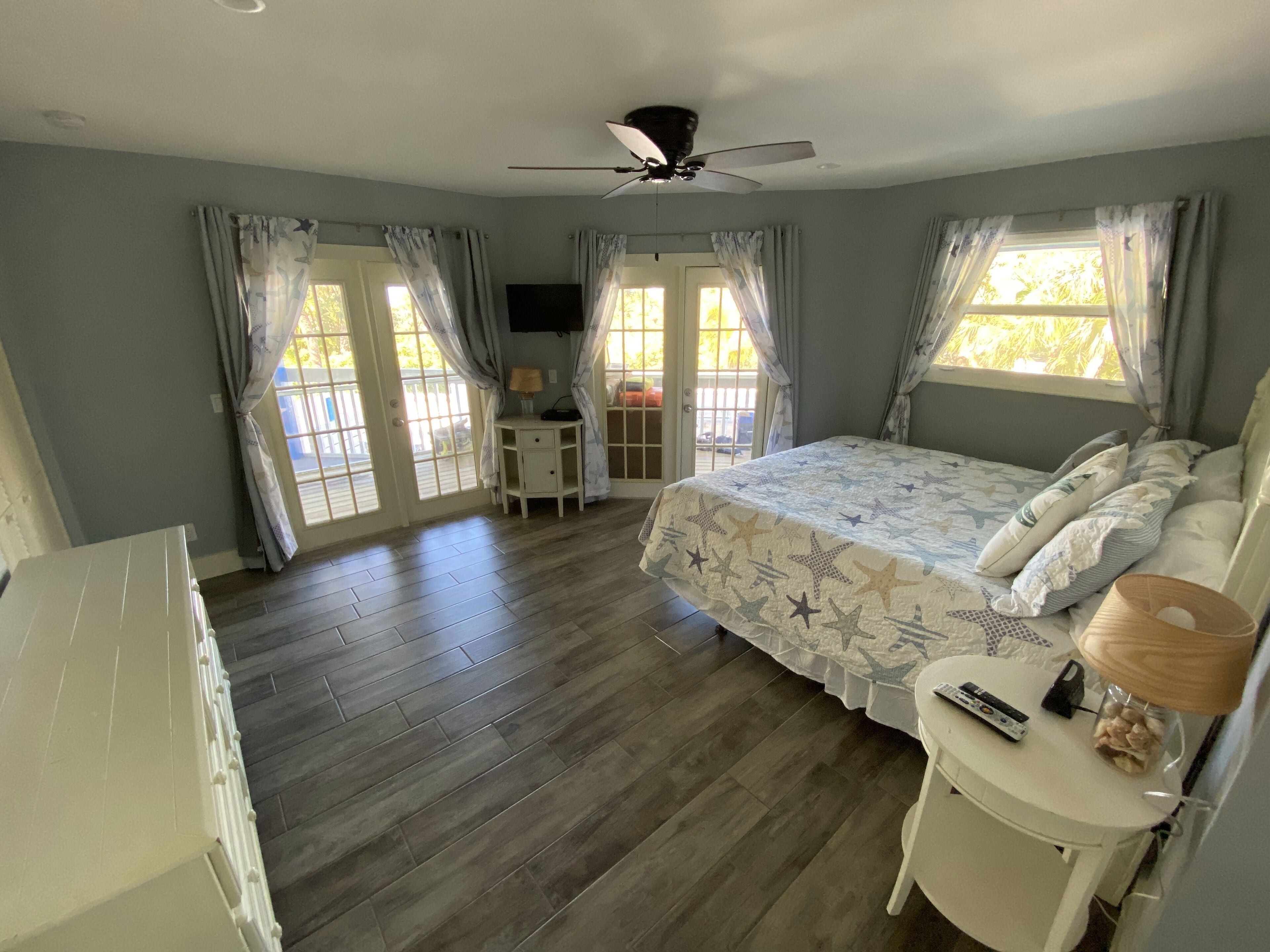 A bedroom with a bed, a desk, a ceiling fan, and a window with curtains.