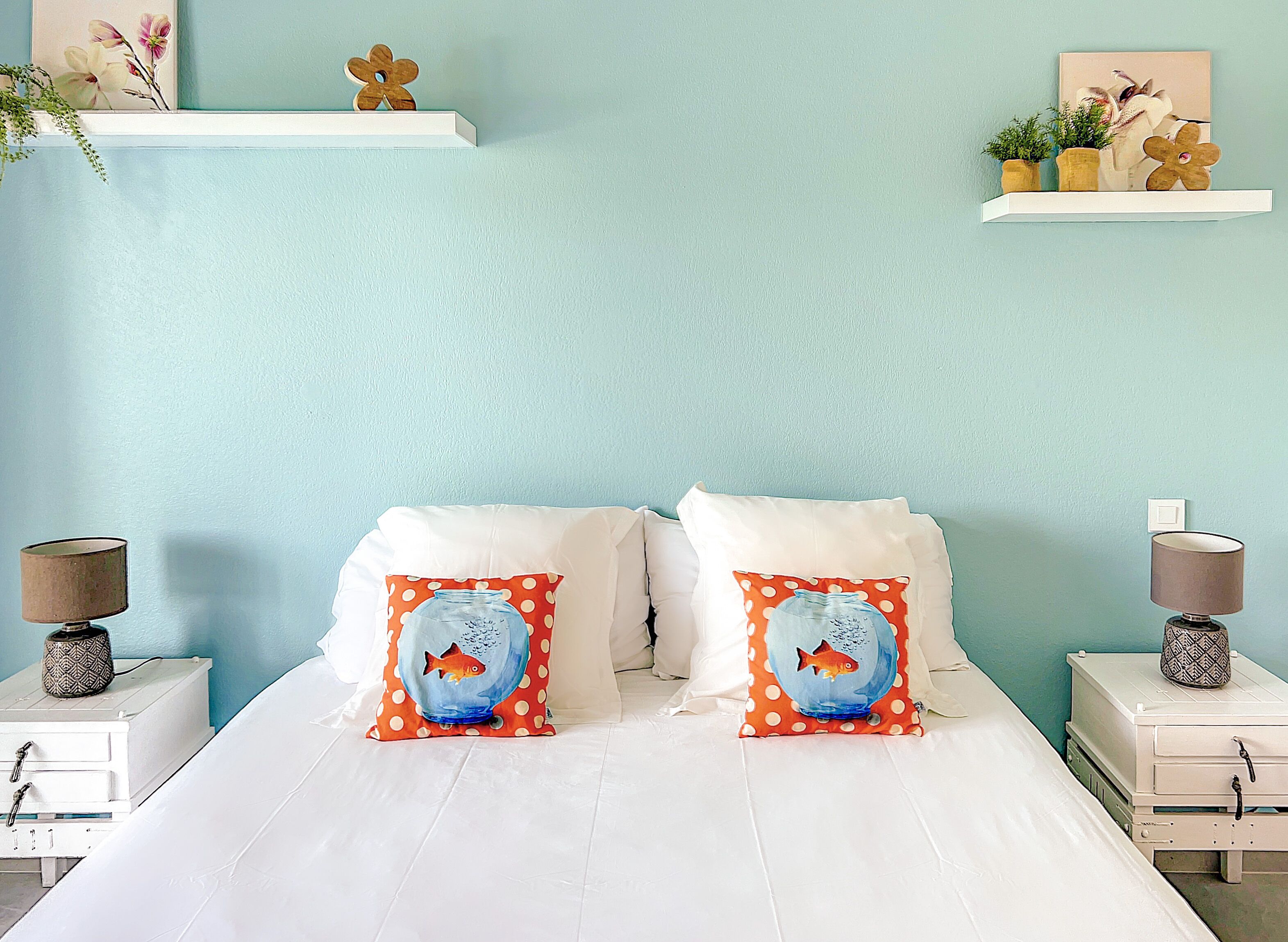 Una cama con ropa de cama blanca, dos almohadas con diseños de peces y dos mesitas de noche con lámparas.